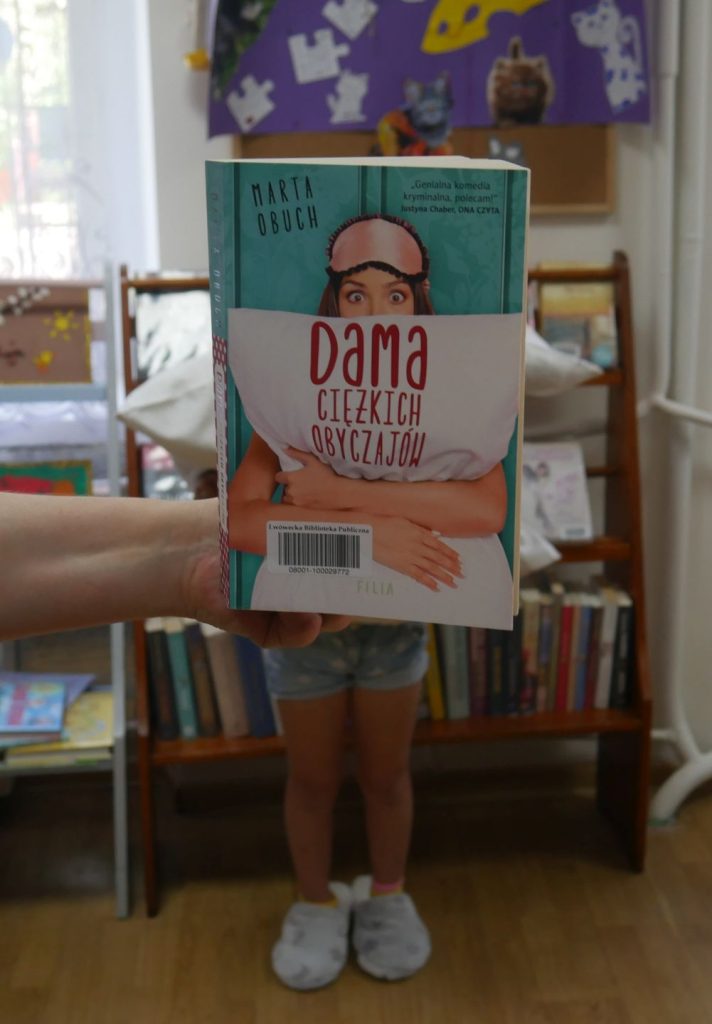Stojąca dziewczynka zasłaniająca twarz książką