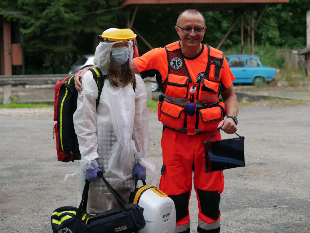 Po prawej mężczyzna w stroju ratownika medycznego i osoba w kombinezonie ratunkowym.
