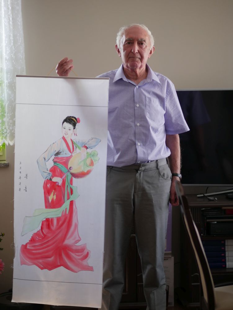 Stojący mężczyzna, trzymający w dłoni obraz z namalowaną kobietą.
