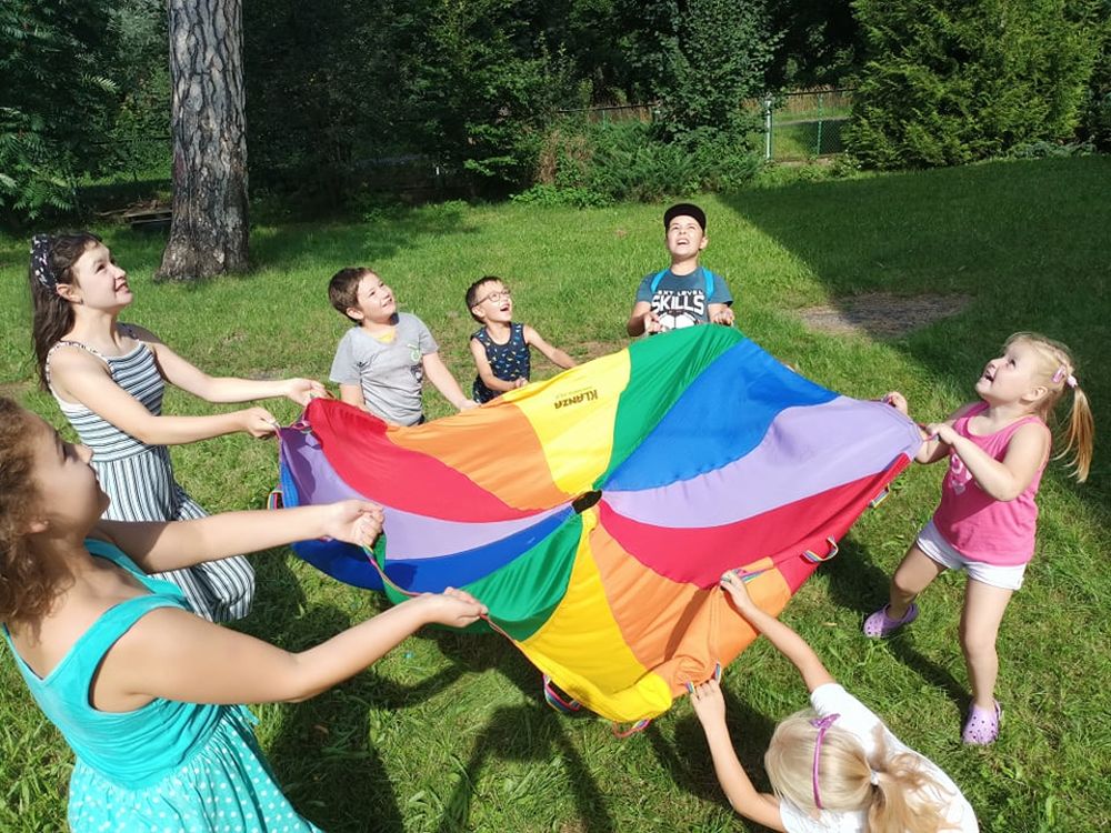Grupa dzieci stojąca na trawie i trzymająca chustę animacyjną