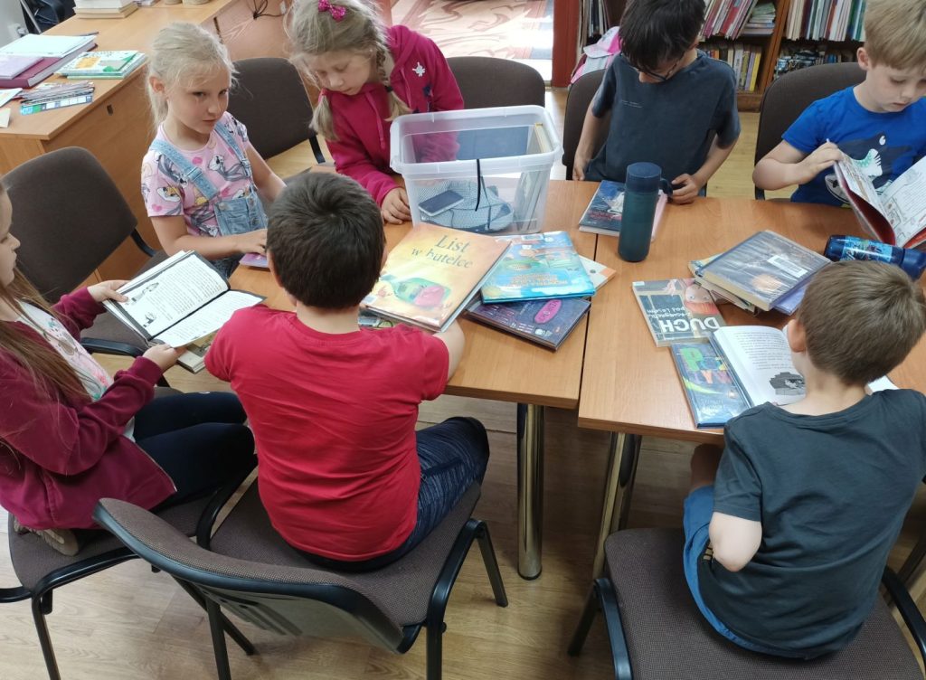 Grupa dzieci siedzi przy stole i przegląda książki