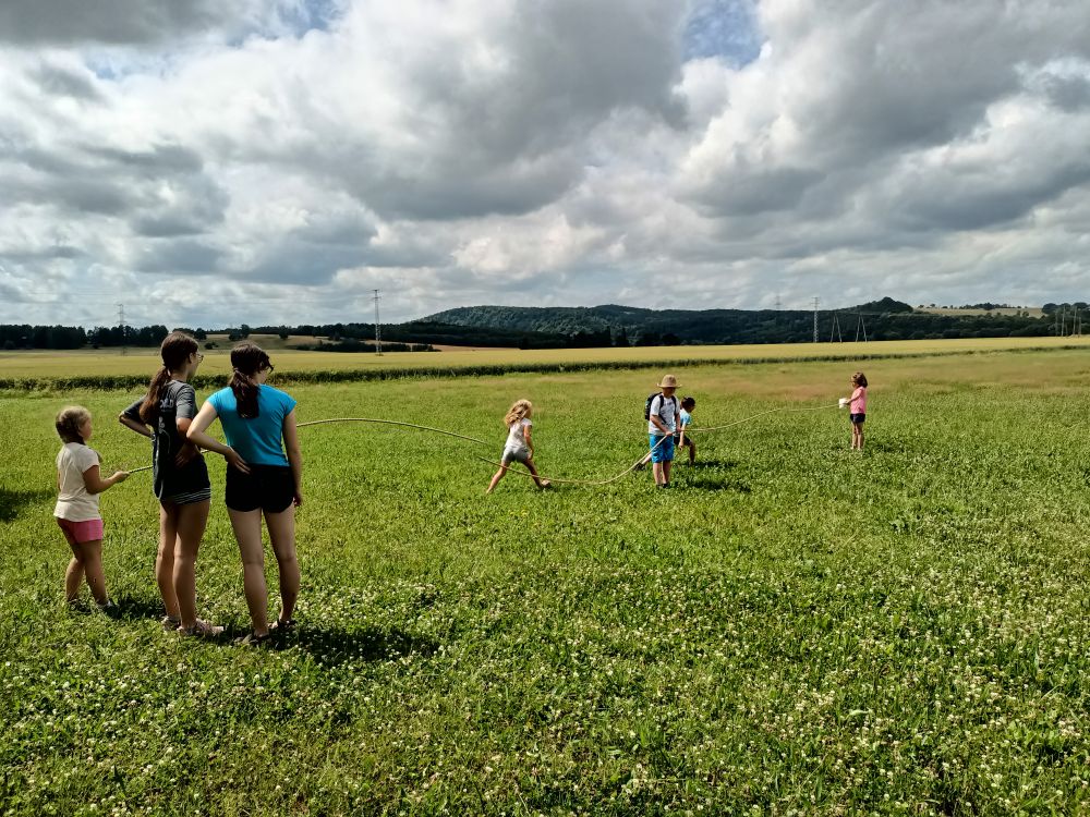 Grupa dzieci stojących na trawie i trzymająca rozciągniętą linę.