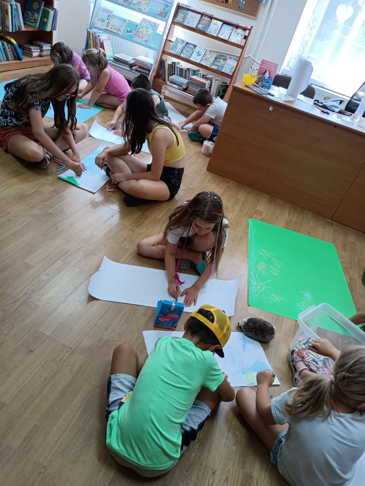 Grupa dzieci siedzących na podłodze i malująca obrazki.
