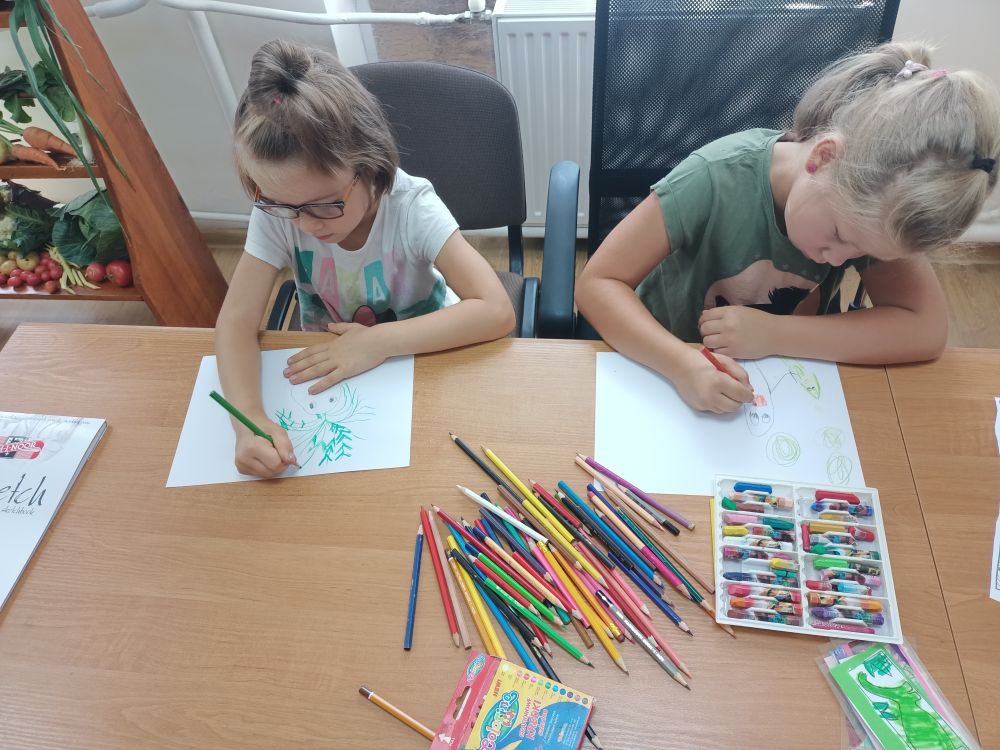 Dwie dziewczynki siedzące przy stole i rysujące obrazki.
