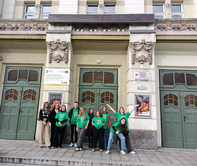 1. Grupa młodych osób w zielonych koszulkach stojąca przed dużym budynkiem.