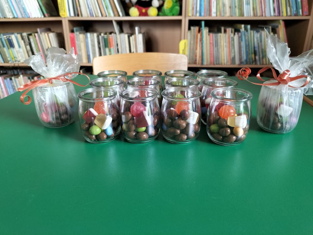 na zielonym stoliku stoją prezenty dla dzieci – 14 słoiczków ze słodyczami, w tle regały z książkami