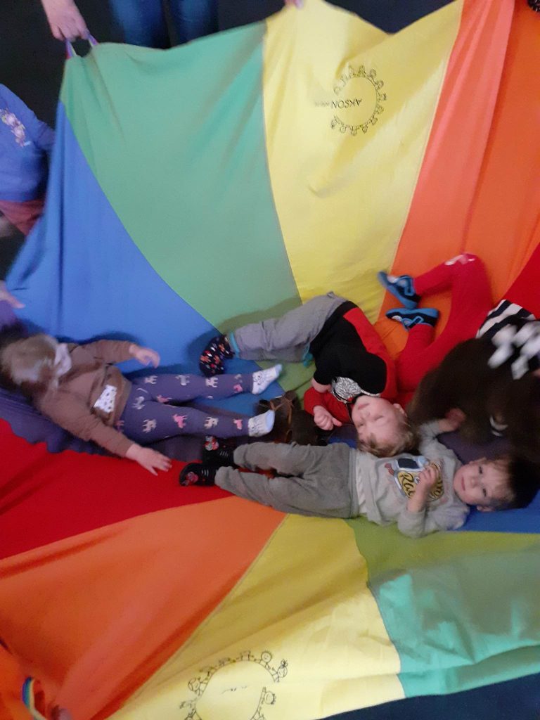 Na środku kolorowej chusty animacyjnej leżą dzieci.