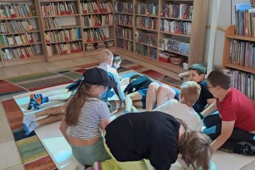 Na podłodze interaktywnej znajduje się grupka dzieci. W tle widać regały z książkami.