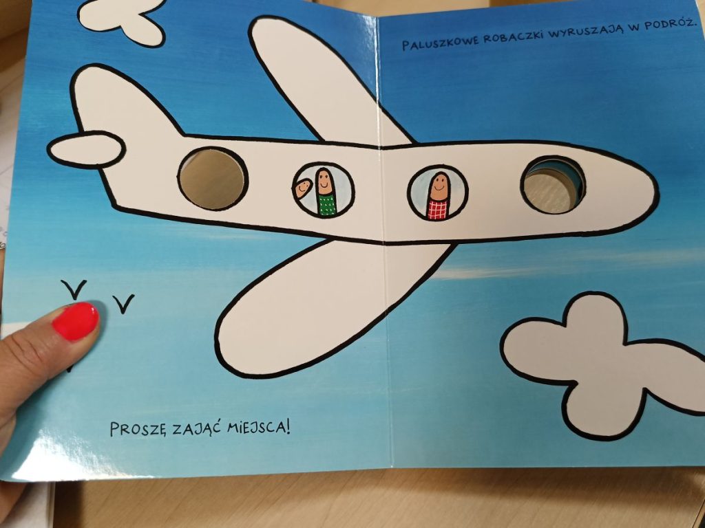 Rozłożona książka. Na środku rysunek samolotu na tle nieba.