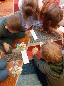 Na kolorowym dywanie siedzą w kółku dzieci. W środku koła leżą małe, kolorowe karteczki z obrazkami i nazwami pór roku.
